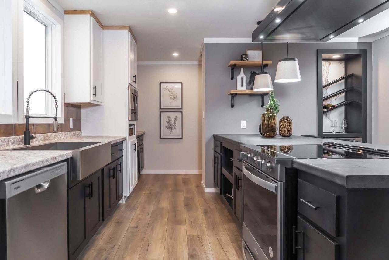 Modern kitchen with black and white cabinets, a gray island, stainless steel appliances, wood flooring, and decorative shelves, creating a sleek and inviting atmosphere.