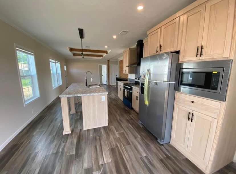 Modern kitchen with light wood cabinetry, stainless steel appliances, and an island with a marble countertop. Bright with large windows and wooden flooring.