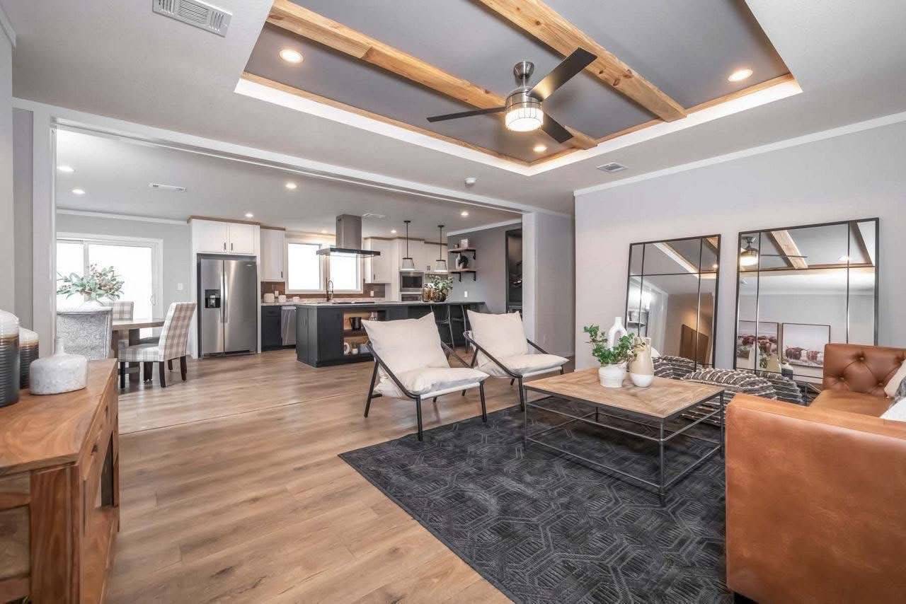 Modern open-concept living room with light wood flooring, beige chairs, a brown leather sofa, and a sleek kitchen. Cozy and inviting ambiance.