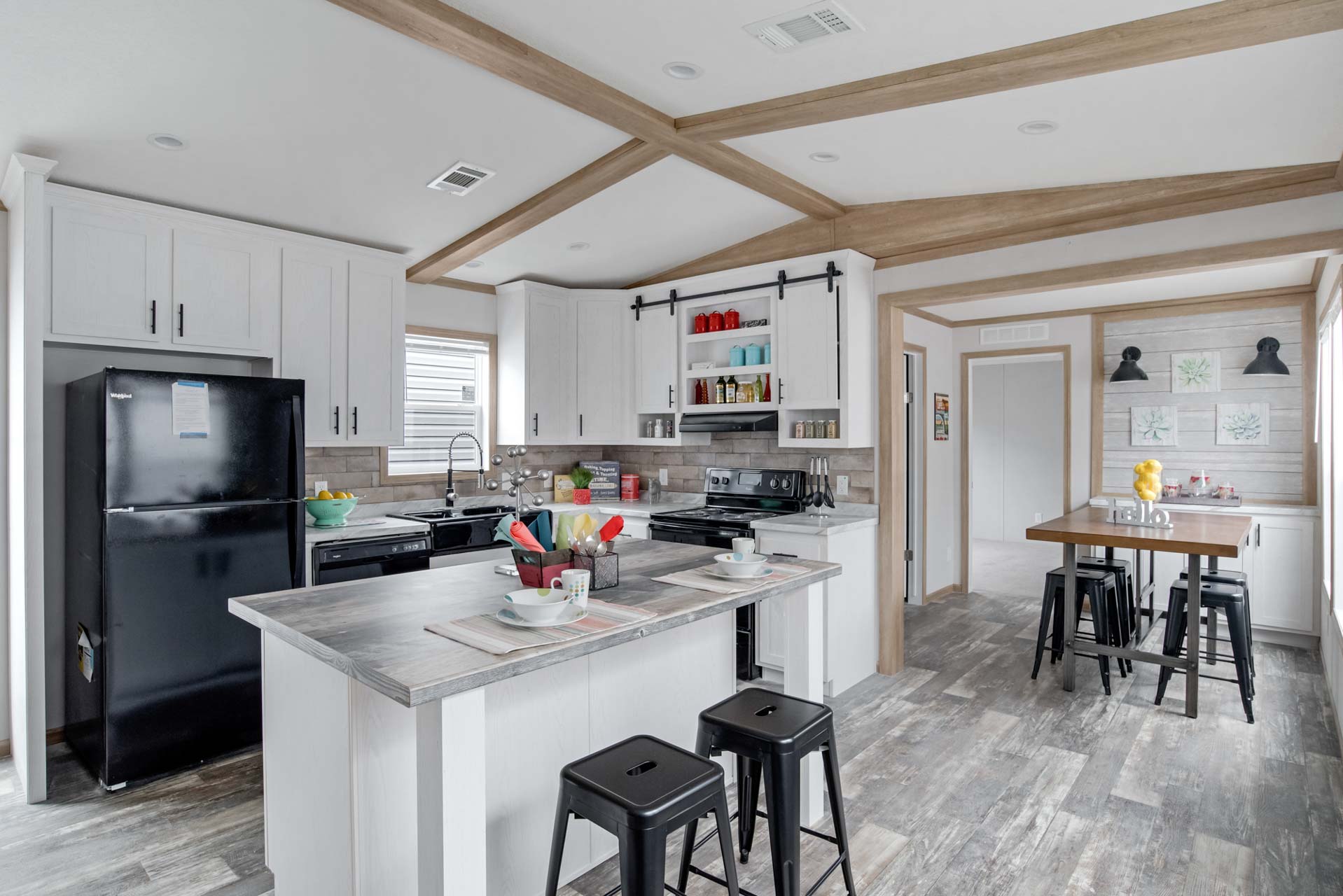 Modern kitchen with a spacious layout, featuring white cabinets, a black fridge, and a central island with stools. Warm wood accents, bright and inviting.