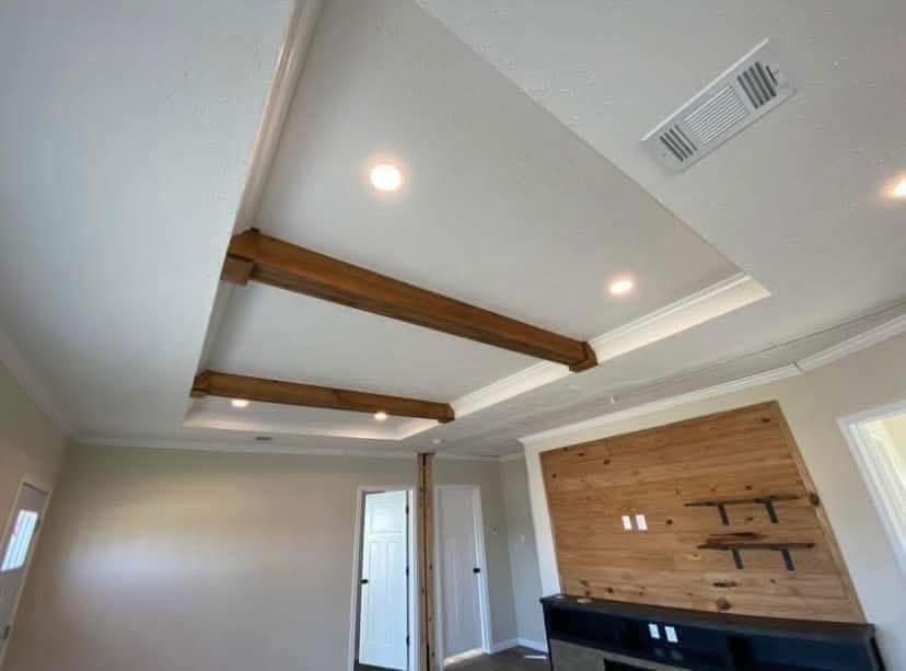 Ceiling view of a room with recessed lighting and wooden beams. A wooden accent wall features shelves. Neutral wall colors create a modern, cozy atmosphere.