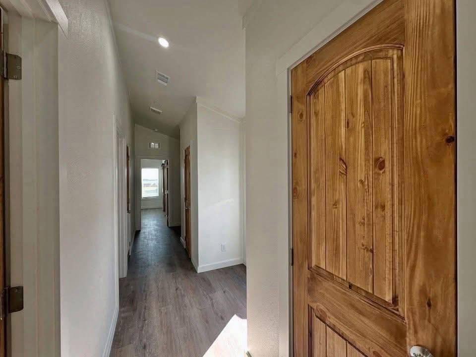 A hallway with light wood flooring and white walls, featuring closed wooden doors on the right. Sunlight streams in, creating a warm, inviting atmosphere.