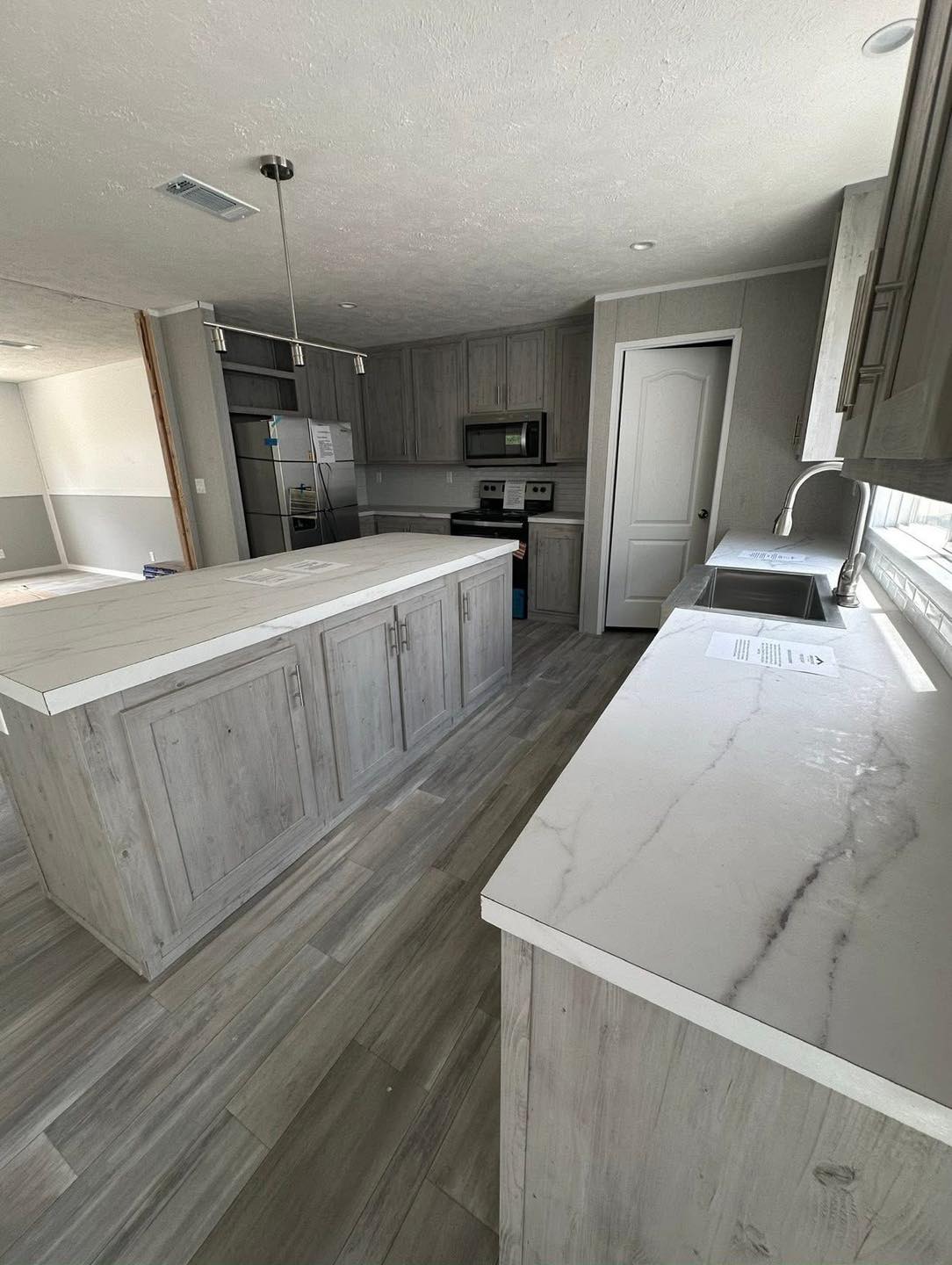 Modern kitchen with light gray wooden cabinetry and marble countertops. Features a central island, stainless steel appliances, and a bright, airy feel.