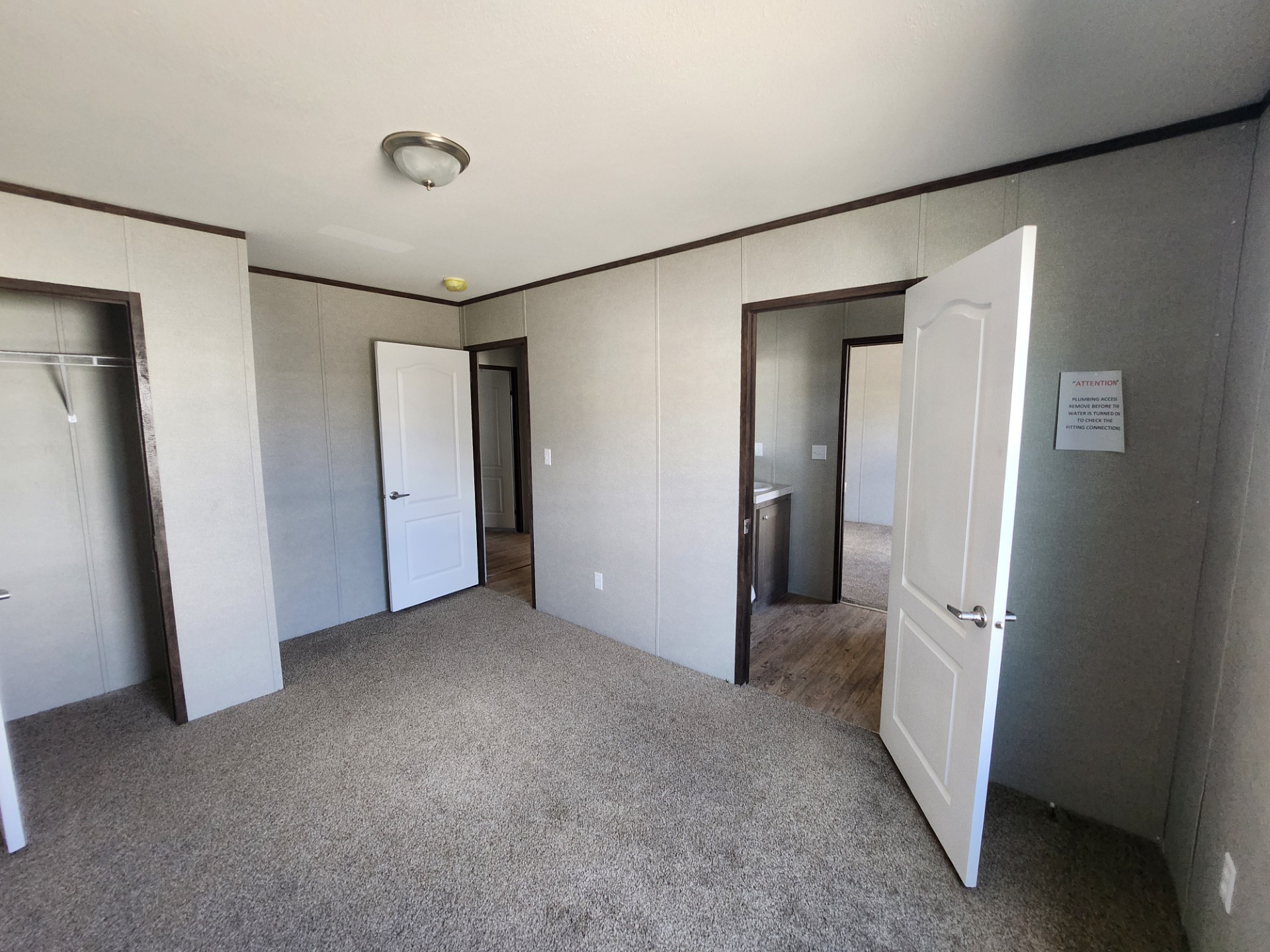 Empty room with beige carpet, gray walls, and three open white doors leading to adjoining rooms. A ceiling light fixture adds a simple touch.