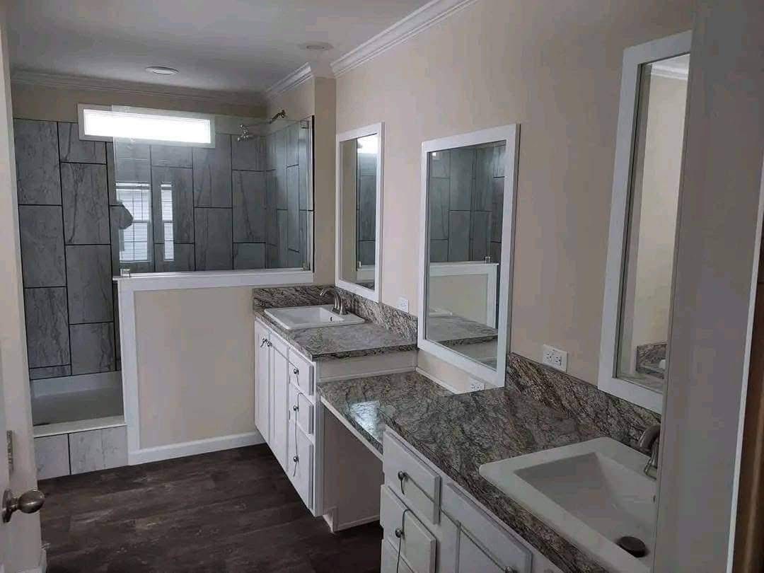Modern bathroom with dual sinks, gray stone countertops, and white cabinetry. Features a large mirror, gray tiled shower, and soft lighting.