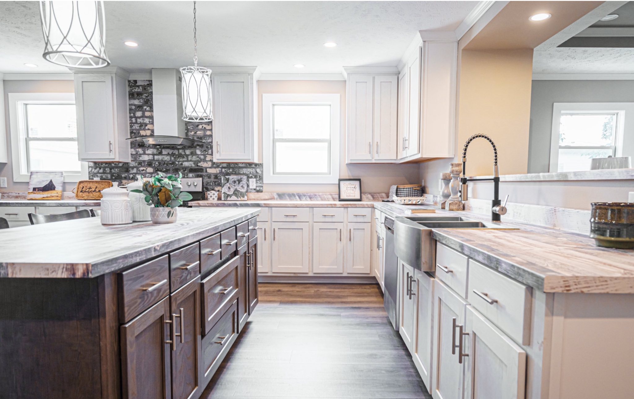 Spacious kitchen with white cabinets, dark wood island, stainless steel sink, and pendant lights. Bright, clean, modern feel with brick backsplash.