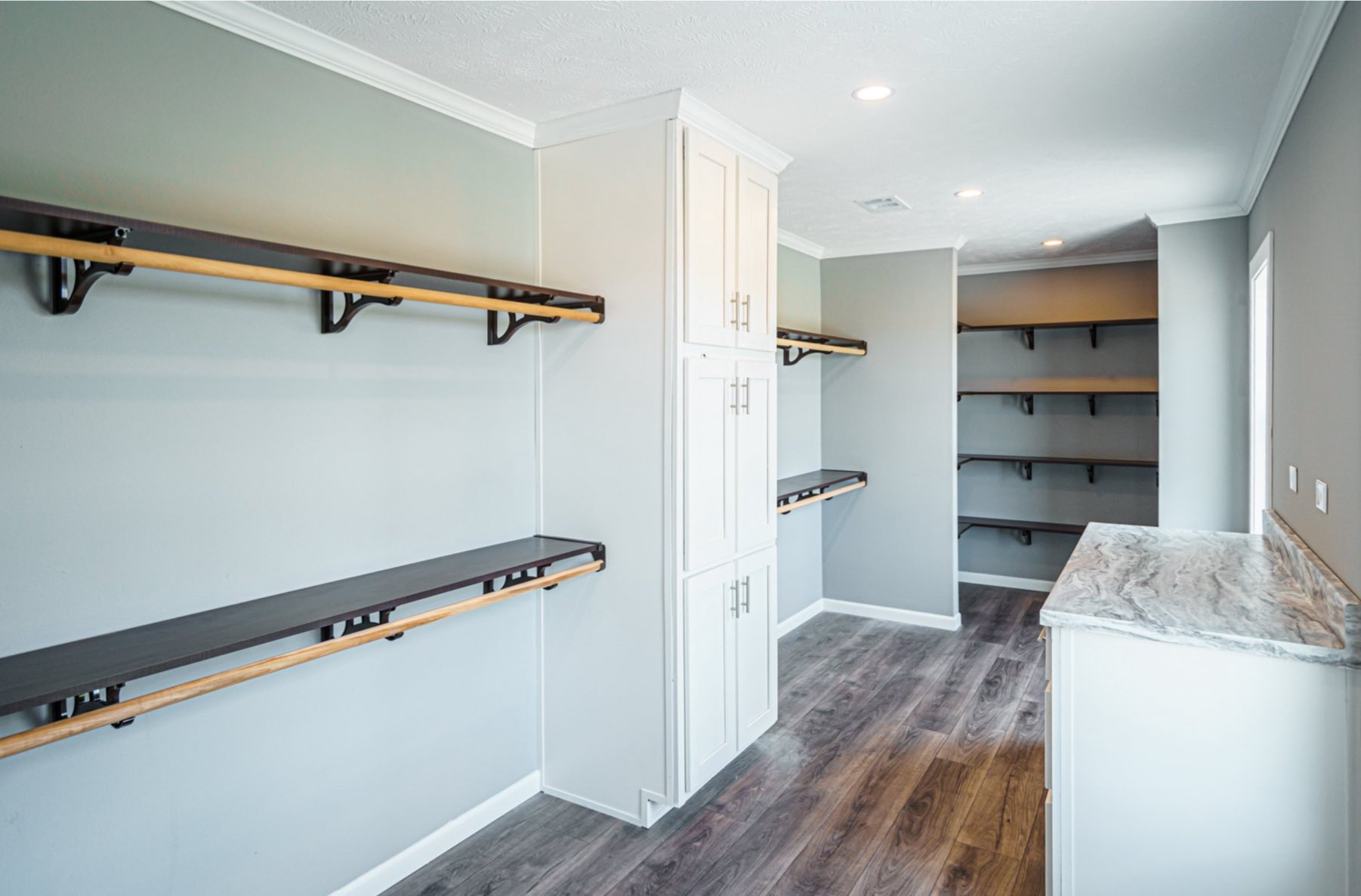 Spacious pantry with grey walls, wooden shelves, and white cabinets. Natural light highlights the dark wood flooring, creating a clean, organized feel.