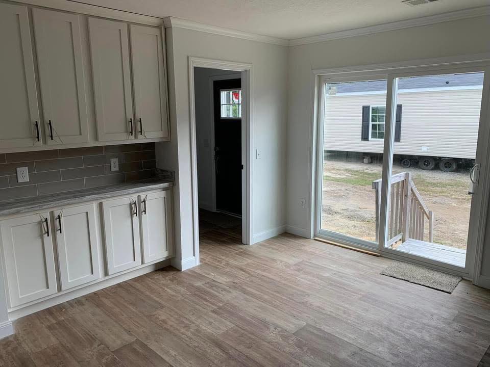 Bright room with light wood flooring, white cabinets, and a sliding glass door opening to a small deck. A mobile home is visible outside.