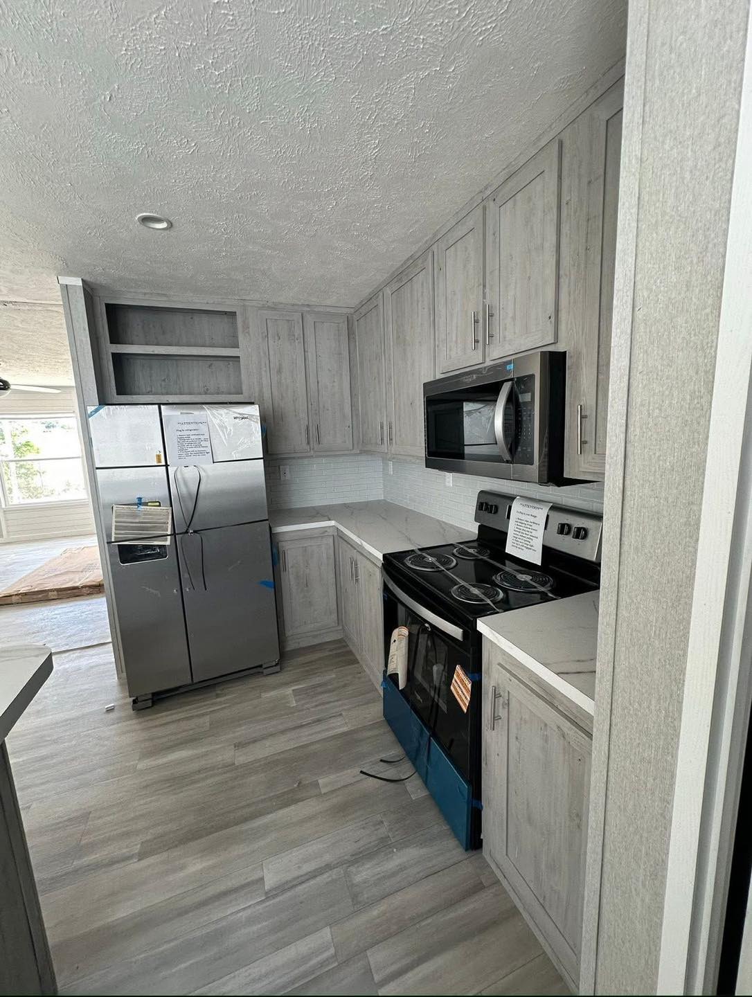 Modern kitchen with light gray wood cabinets, stainless steel appliances including a fridge and microwave, and a smooth surface stove. Bright and minimalistic.