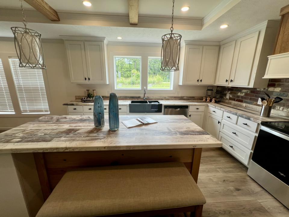 Spacious kitchen with white cabinets, marble countertops, and a wood-beamed ceiling. Central island holds two blue vases and an open book. Bright, airy vibe.