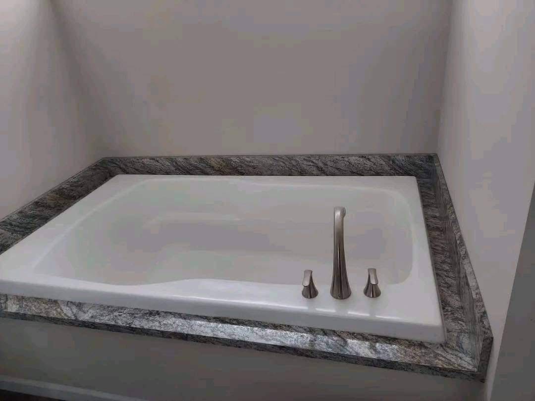 A rectangular bathtub with a modern faucet is set into a granite countertop. The surrounding walls are light, creating a calm and clean atmosphere.