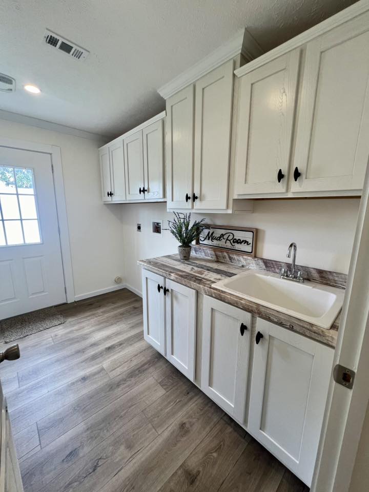Laundry room with white cabinetry, marble countertop, and a sink. A "Mud Room" sign and plant sit on the counter. Bright and tidy atmosphere.