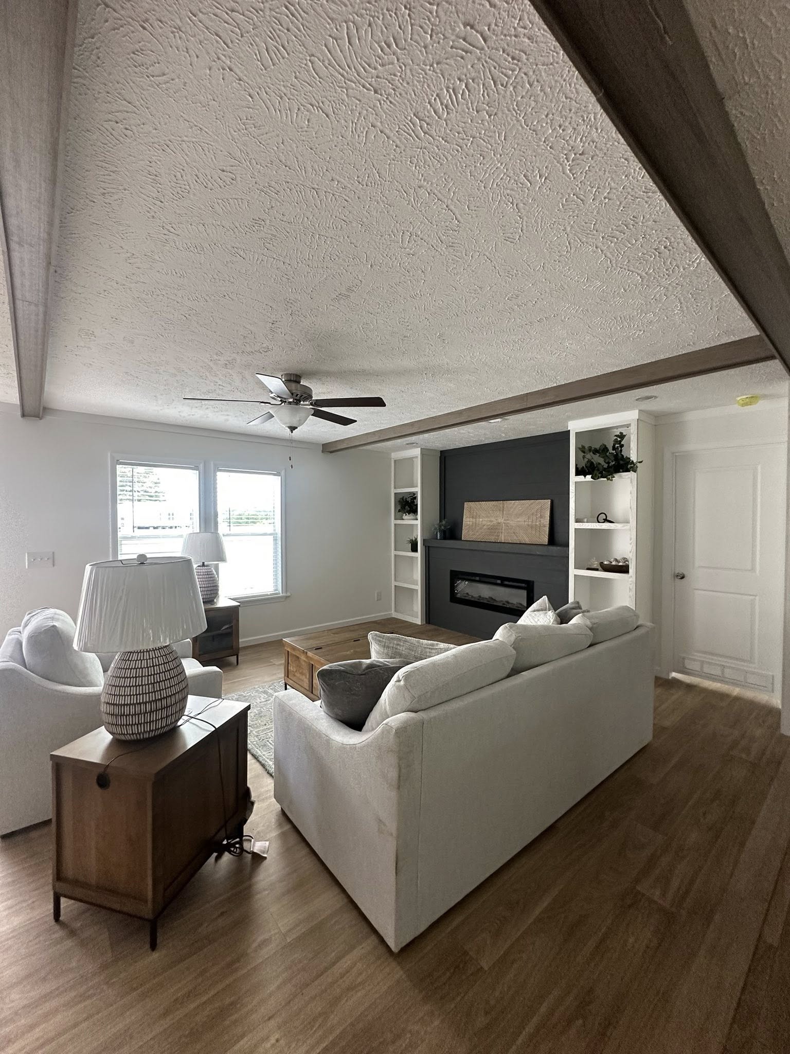 Cozy living room with white couches, a light wood floor, and built-in shelves. A fireplace is centered on a dark accent wall, emitting a cozy vibe.