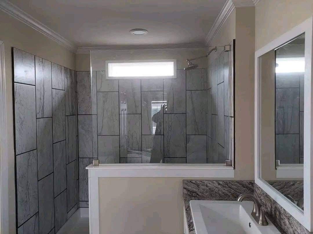 Modern bathroom with gray tiled shower, glass partition, rectangular window, and white sink with a marble countertop. Bright and minimalist design.