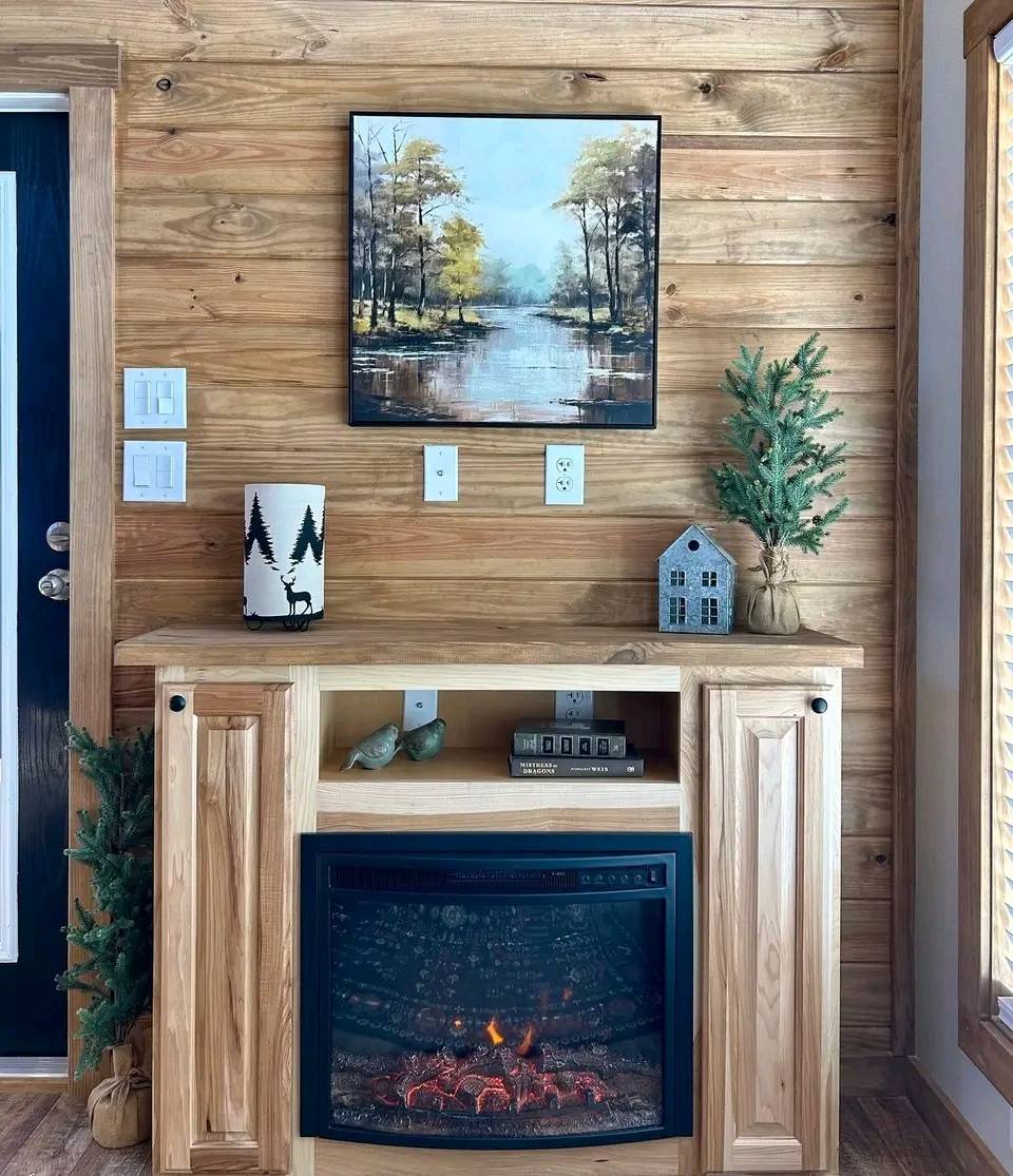 Cozy room with a wood-paneled wall featuring a landscape painting. Below, an electric fireplace, small decor items, and a potted tree create a warm ambiance.