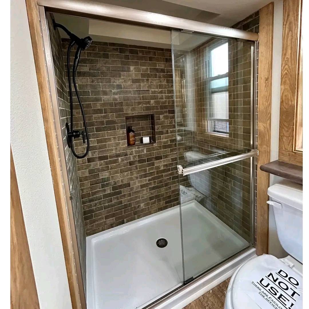 Spacious shower with brown brick tiles, black showerhead, glass doors, and built-in shelf. Adjacent toilet with a "Do Not Use" sign on the lid.