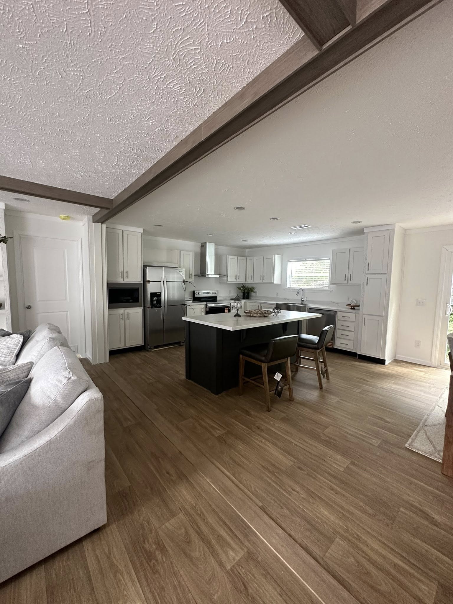 Modern kitchen with white cabinets, stainless steel appliances, and a central island with barstools. Light wood flooring and a cozy adjacent living area.