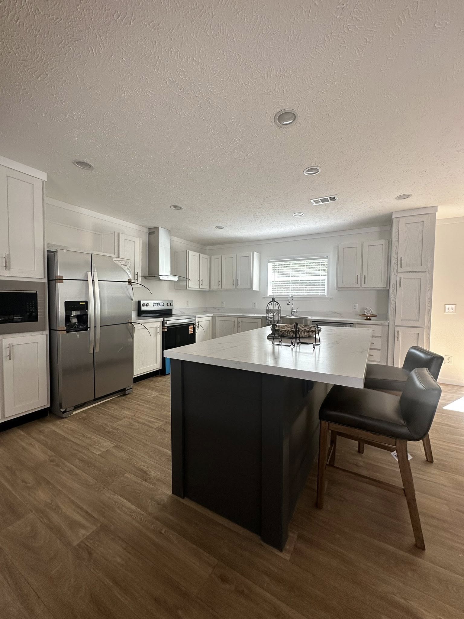 Modern kitchen with white cabinets, stainless steel appliances, and a large island. Light wood flooring and soft natural light create a cozy ambiance.
