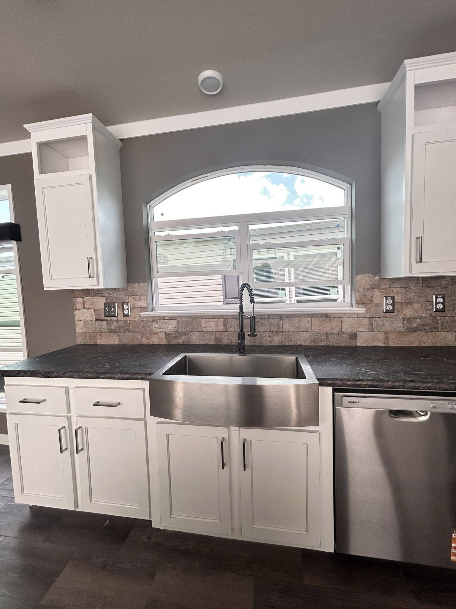 Stylish kitchen with white cabinets, stainless steel farmhouse sink, and black countertop. A large window with an arched top allows natural light in.