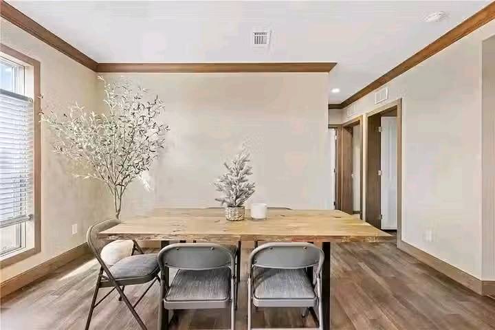Cozy dining area with a wooden table, two metal chairs, and a decorative plant. Bright room with light walls, wooden floors, and natural lighting.