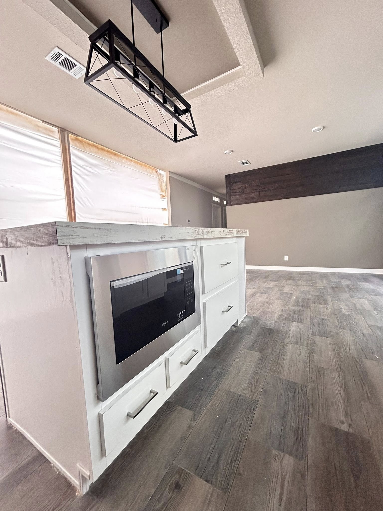 Modern kitchen with white island, built-in microwave, and pendant light. Gray wood flooring and neutral walls create a sleek, airy atmosphere.