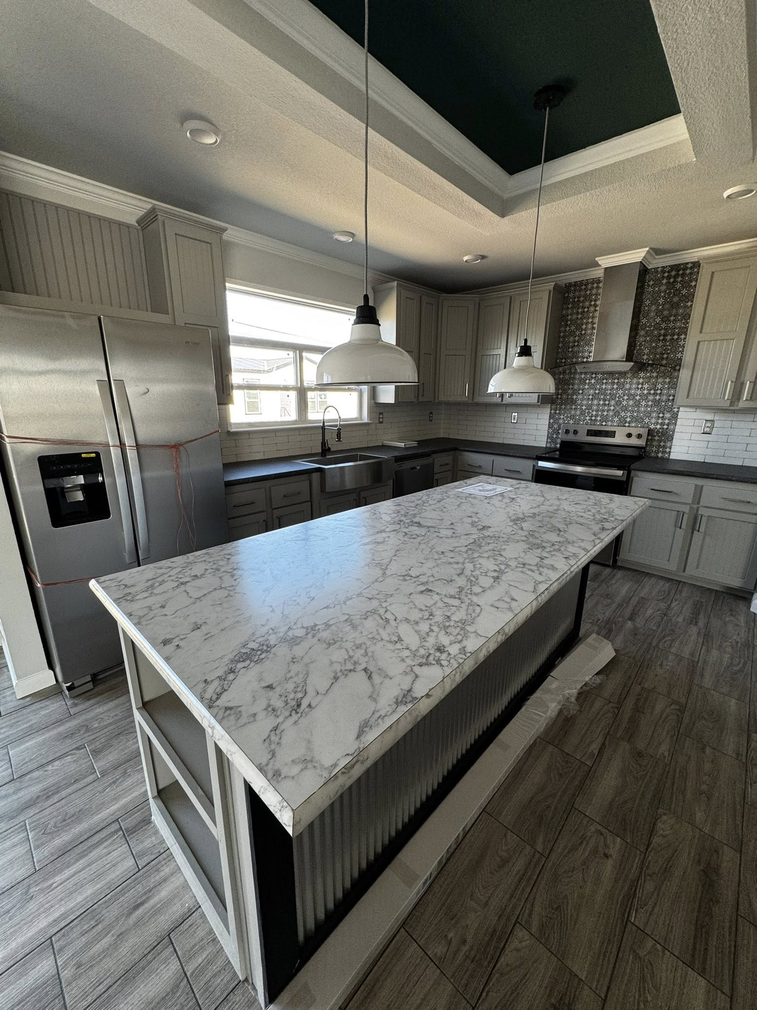 Modern kitchen with marbled island countertop, stainless steel appliances, gray cabinets, and pendant lights, creating a sleek and inviting atmosphere.