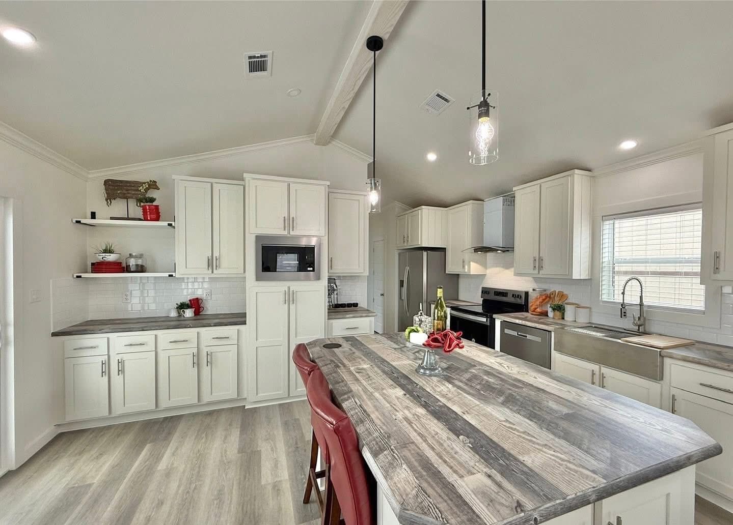 Spacious, modern kitchen with white cabinets, a large wooden island with red stools, pendant lights, and stainless steel appliances. Bright and inviting.