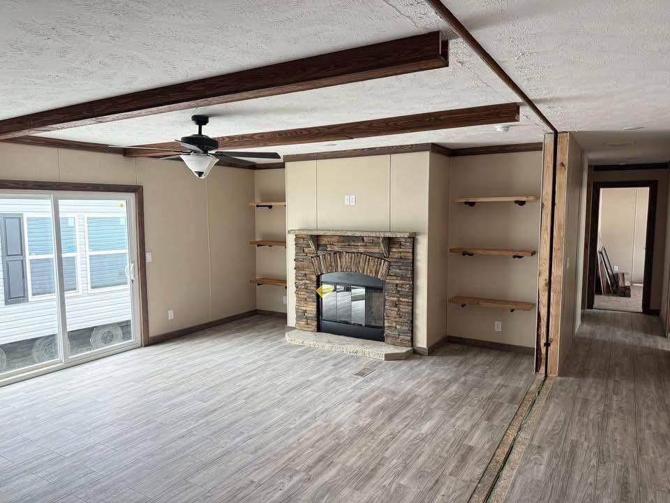 Spacious living room with a stone fireplace, wood beams, and built-in shelves. Light wood floors and large sliding glass doors create an airy feel.