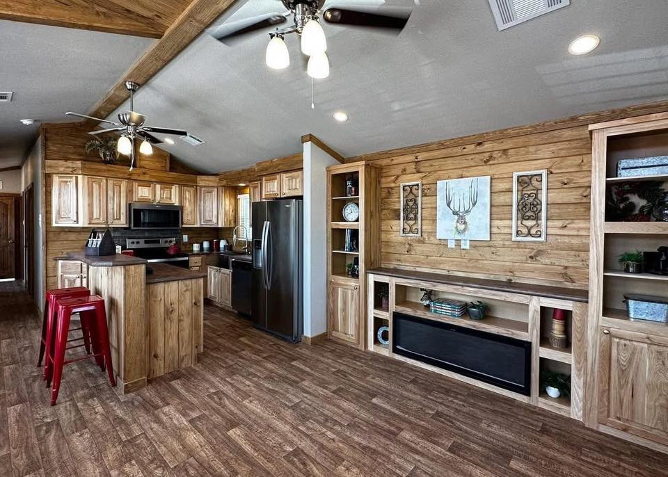 Rustic kitchen with wood paneling and beams, stainless steel appliances, and an island with red stools. Cozy, warm atmosphere with modern touches.