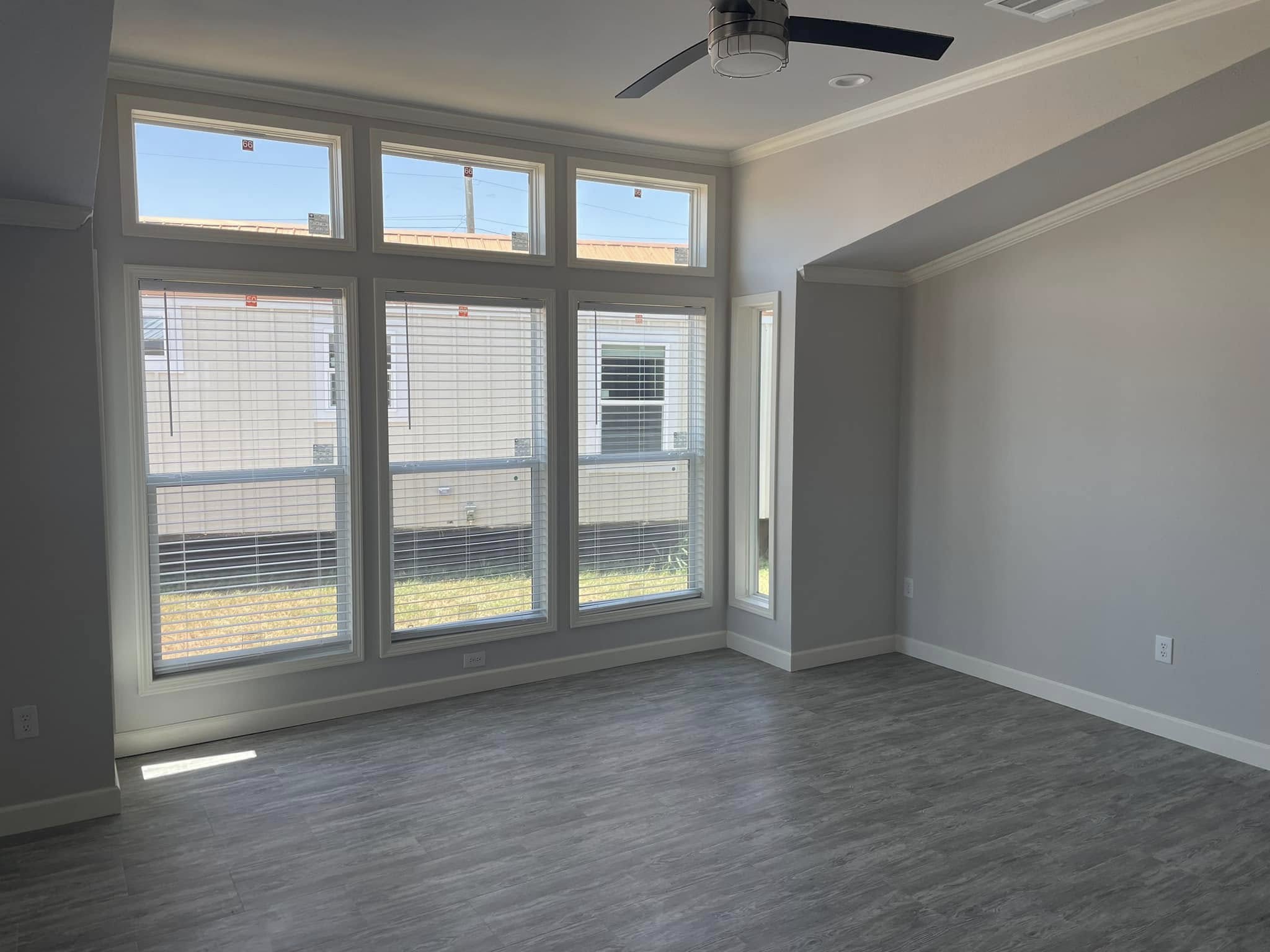 Spacious room with light gray walls and wood floors, large square windows letting in natural light, and a ceiling fan, creating an airy feel.