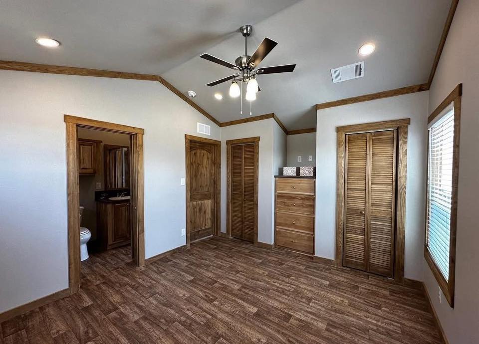 Cozy room with wood accents. Features include a ceiling fan, wood-paneled floors, a chest of drawers, and doors leading to a bathroom and closet.