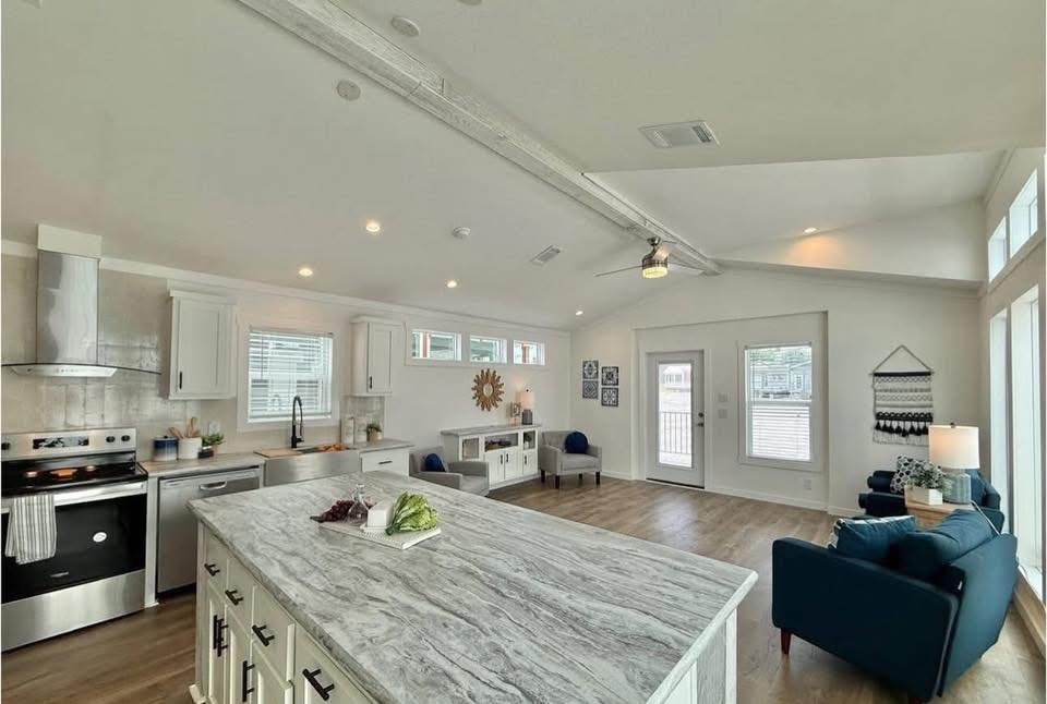 Bright, open-concept living space featuring a kitchen with a marble island and stainless steel appliances. Cozy seating area with blue chairs.