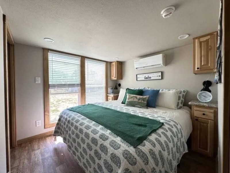 Cozy bedroom with a large bed, patterned bedding, and green accents. Light wood furniture, large windows, and a serene, bright atmosphere.
