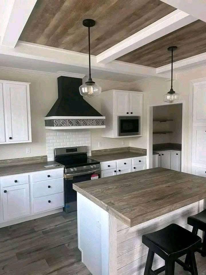 Modern kitchen with white cabinets, wood island, and black stools. Features a black stove hood, hanging pendant lights, and subway tile backsplash. Cozy and clean design.