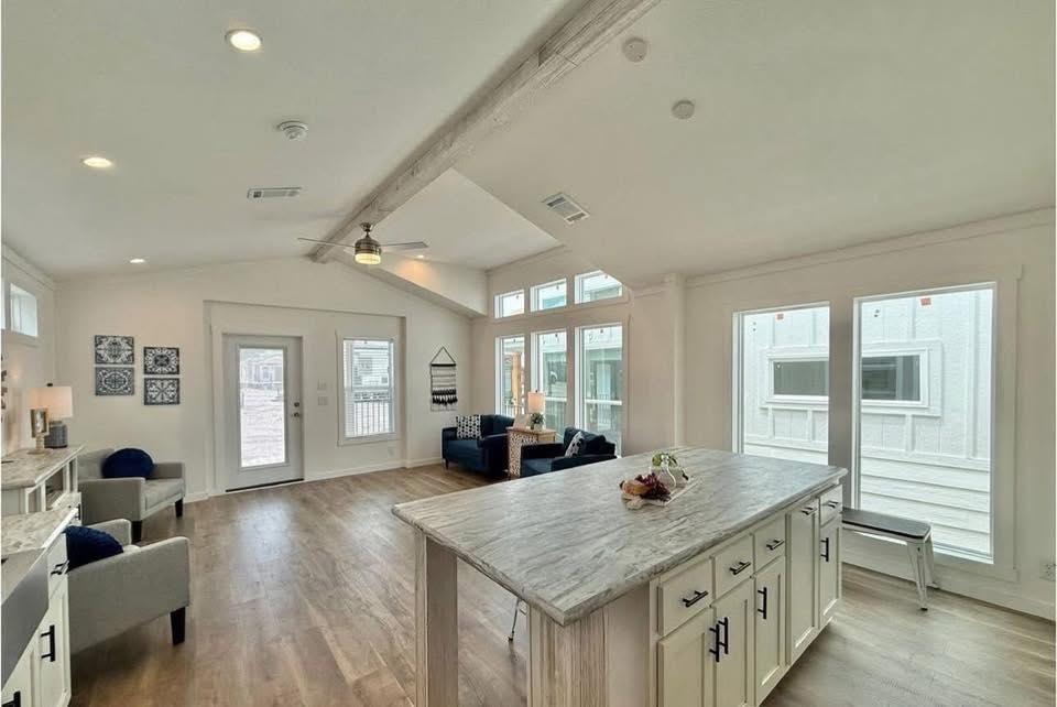 Spacious living area with light wood flooring, high ceilings, and large windows. Features a marble kitchen island and cozy seating with blue armchairs.