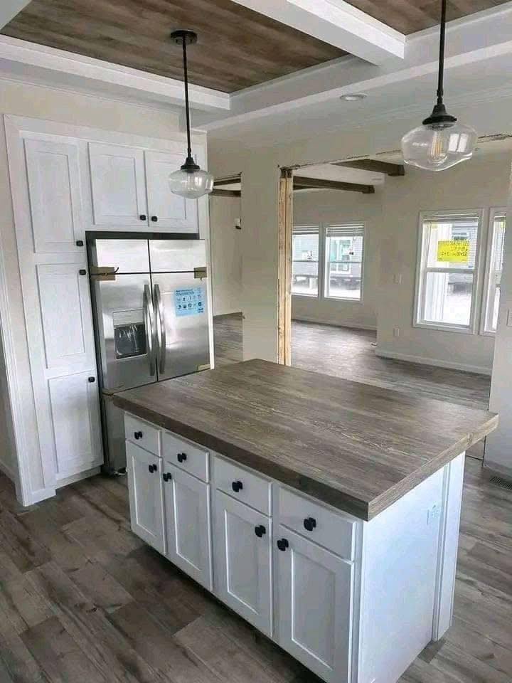 Modern kitchen with a rustic wood-themed island and pendant lighting. Stainless steel fridge and bright windows create an inviting ambiance.