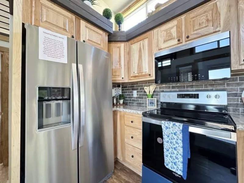 A modern kitchen with stainless steel appliances, including a double-door fridge and oven. Light wood cabinets contrast with dark tiled backsplash.