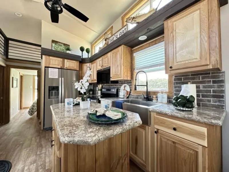 Warm kitchen interior with light wood cabinets, marble countertops, and stainless steel appliances. A central island has decorative dishes. Modern and inviting.