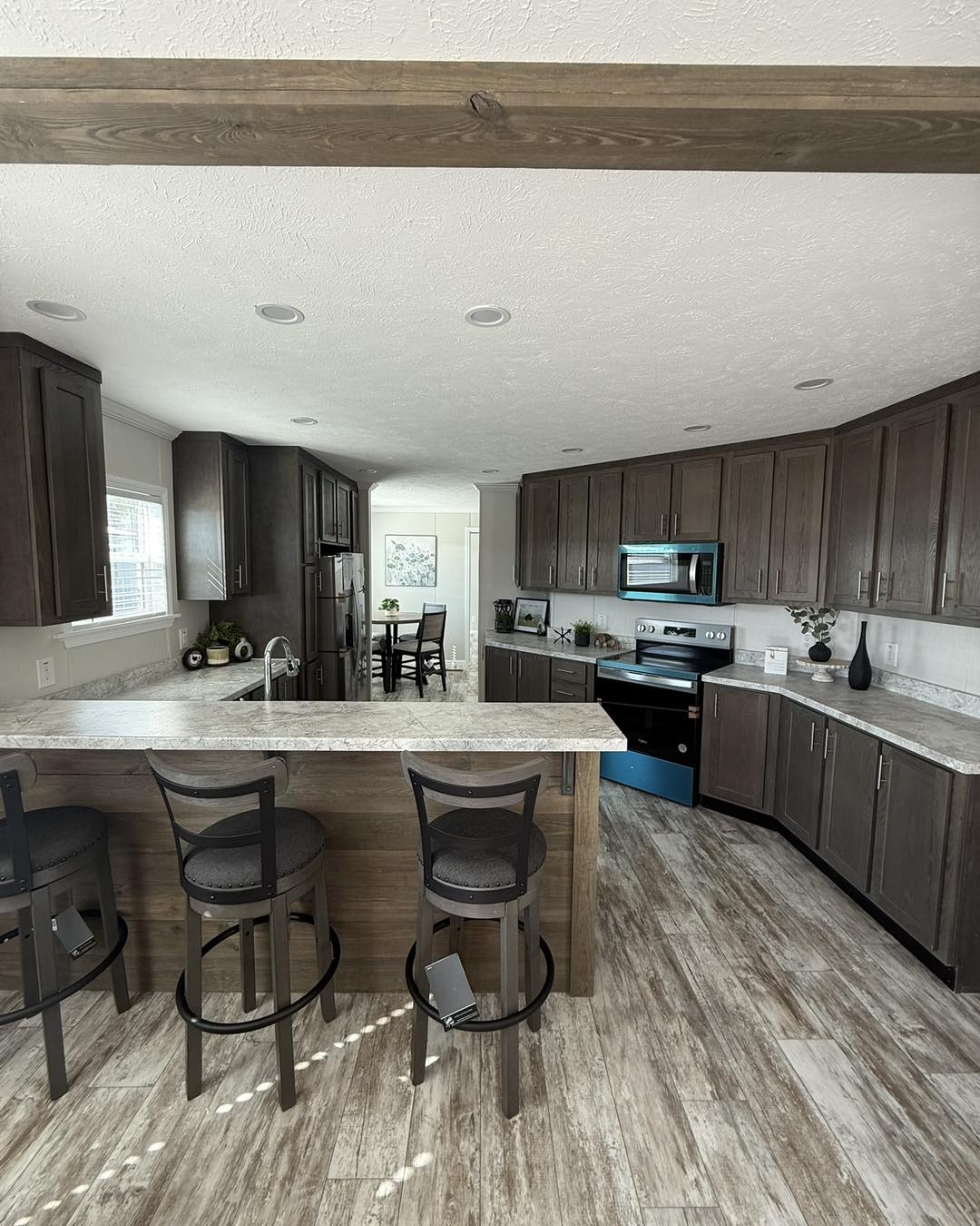 Modern kitchen with dark wood cabinets, marble countertops, and light wood flooring. Island with bar stools, stainless steel appliances, and bright windows.