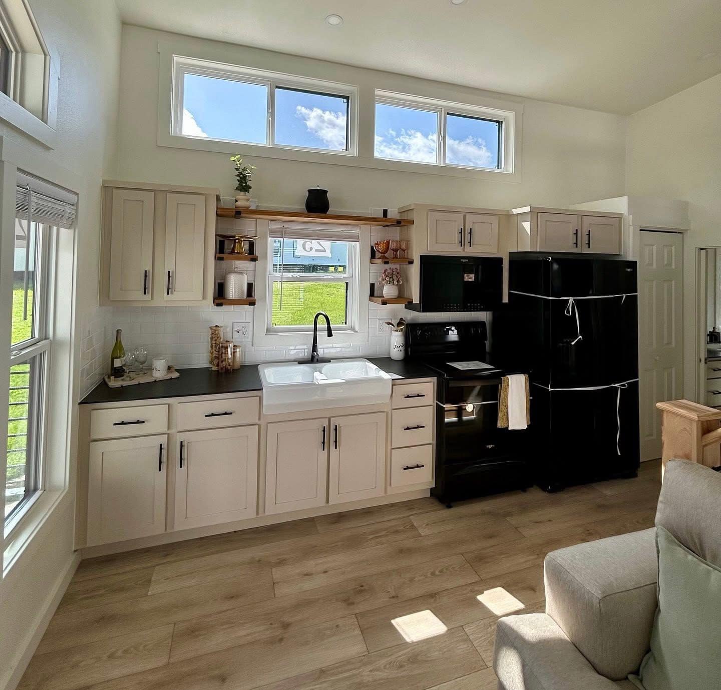 Bright kitchen with cream cabinets, black countertops, and a farmhouse sink. A black stove and fridge are on the right. Windows let in natural light.
