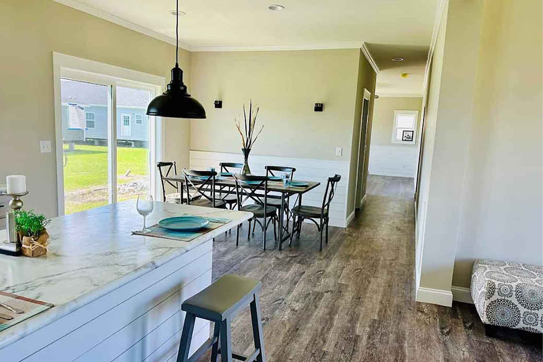 Modern open-concept dining area with a marble island, black pendant lamp, wooden floor, and a window view. Table set for six, creating a cozy atmosphere.