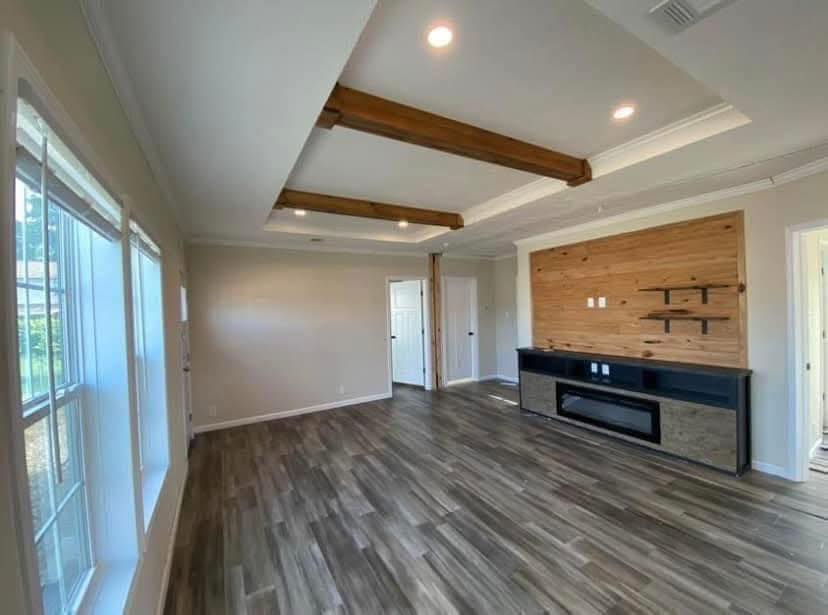 Spacious living room with wood flooring, a wood-accented wall, and modern black entertainment console. Large windows let in natural light. Cozy and inviting.