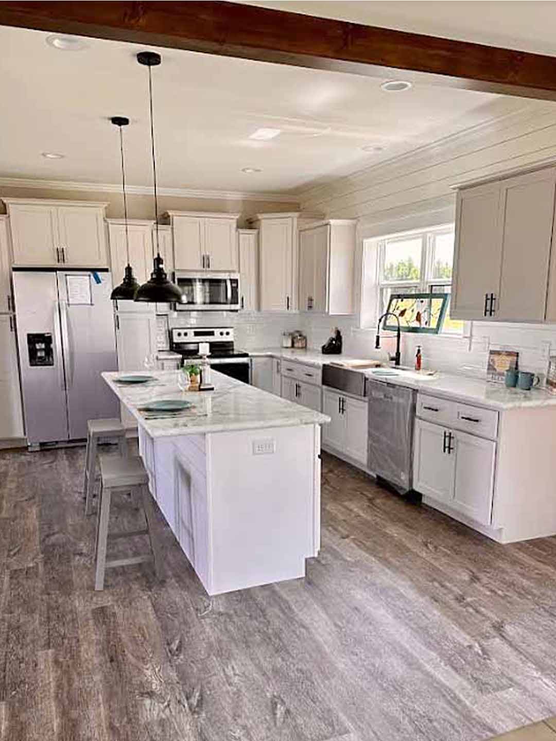 Modern kitchen with white cabinets, stainless steel appliances, and a marble island. Wooden floors and pendant lights create a warm, inviting atmosphere.