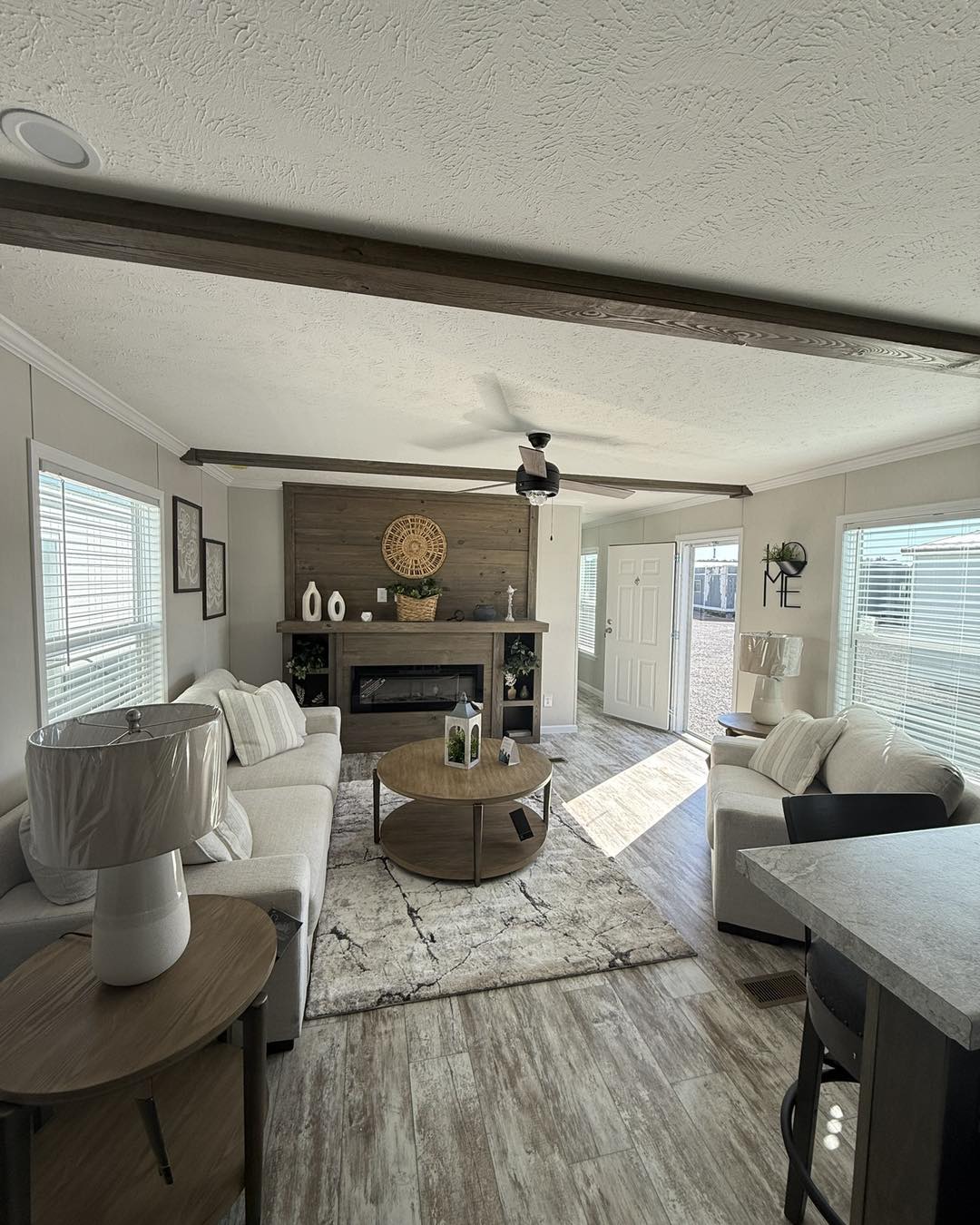 Modern living room with neutral tones and wood accents. Includes a cozy sofa, round coffee table, decorative fireplace, and large windows. Bright and inviting.