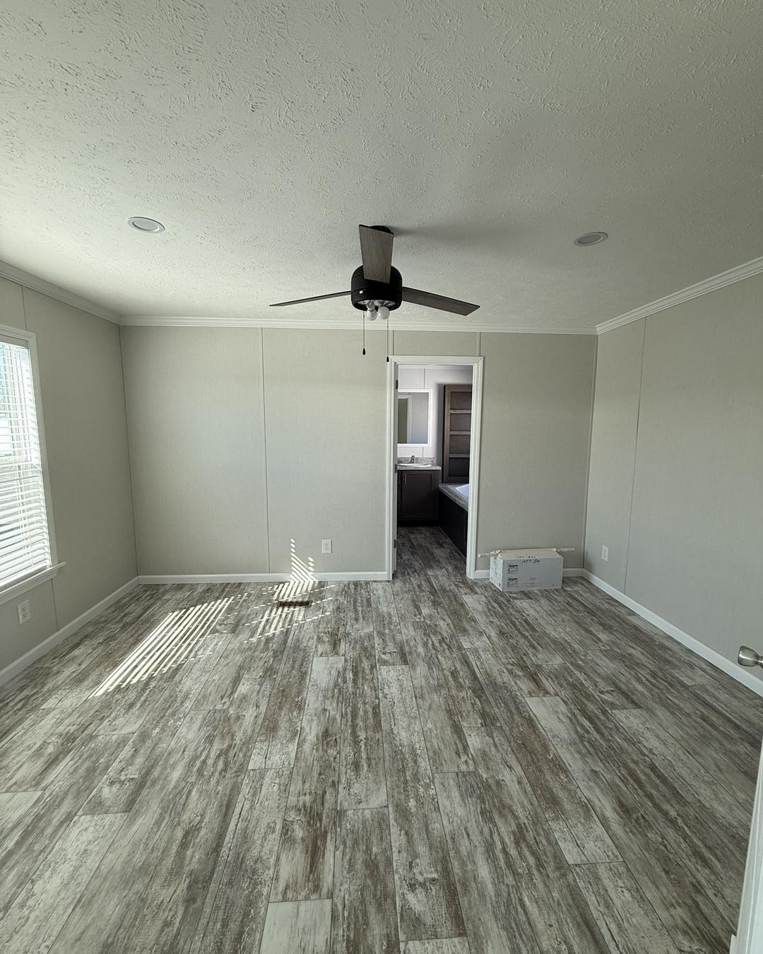 Hallway with light beige walls and wood-patterned floor tiles. Two doorways lead to a walk-in closet and a bathroom with a ceiling fan. Bright and modern.