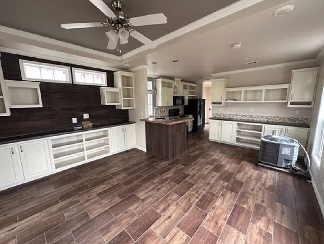 Spacious modern kitchen with dark wood floors, white cabinets, and a central island. An overhead ceiling fan adds to the sleek, minimalistic design.