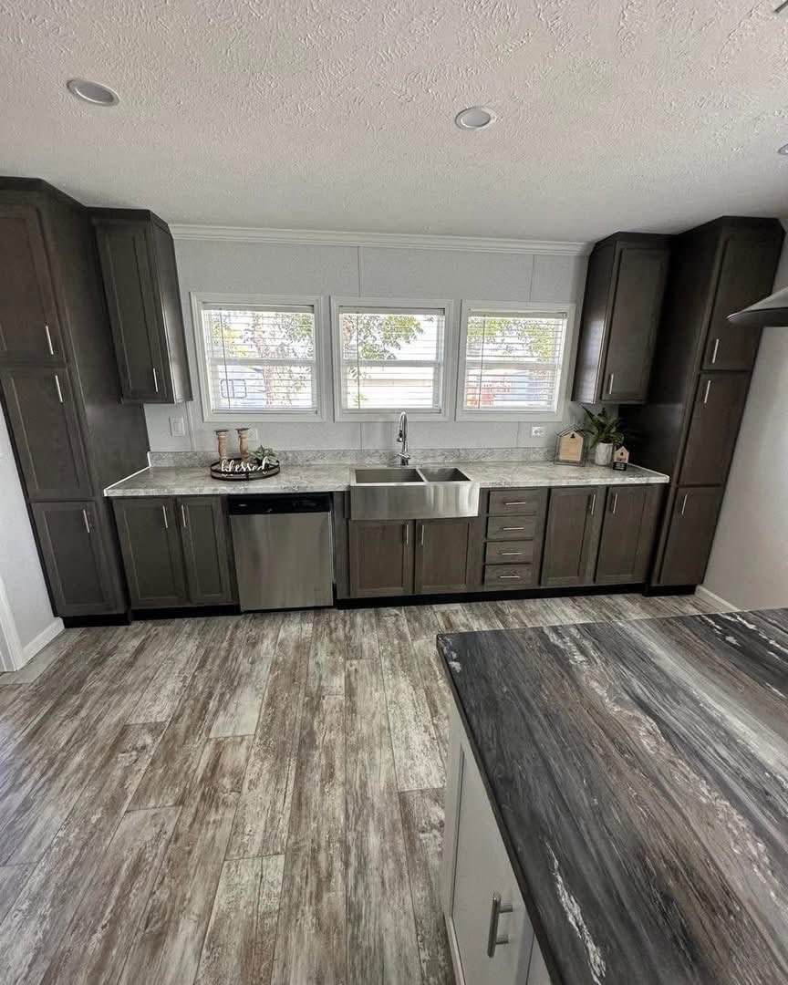 Modern kitchen with dark wood cabinets, stainless steel sink and dishwasher. Light wood-flooring and white countertops add a bright, clean feel.