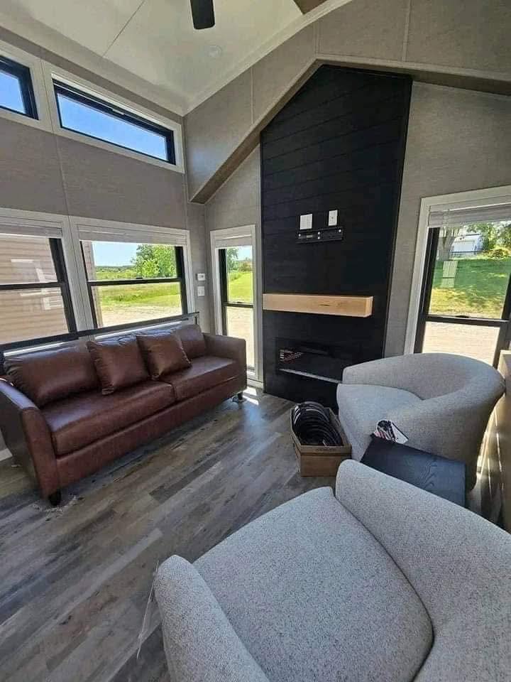 Modern living room with high ceilings, featuring a leather sofa, light gray armchairs, and large windows. A stylish black accent wall adds contrast.