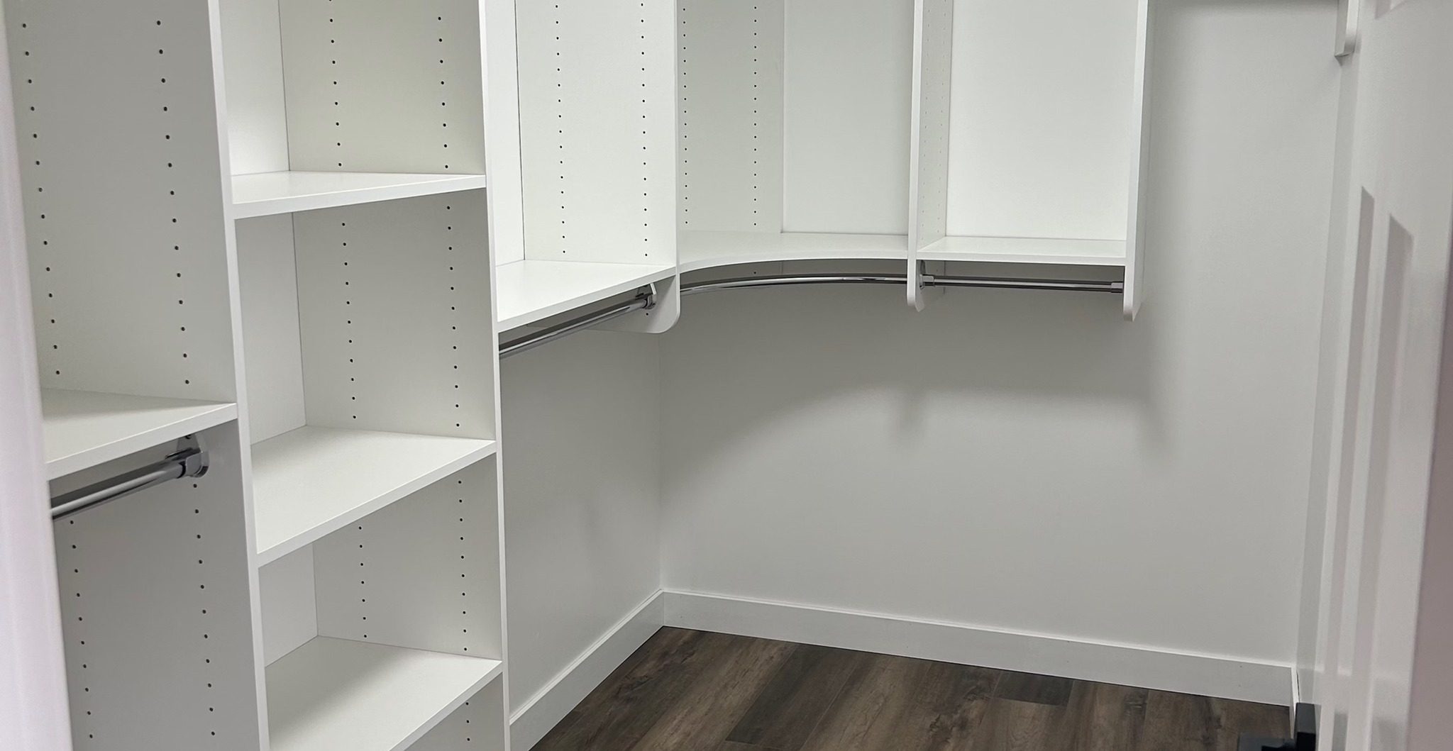 Spacious, empty walk-in closet with white shelving, hanging rods, and dark wood flooring. The clean, organized space conveys a modern, minimalistic feel.