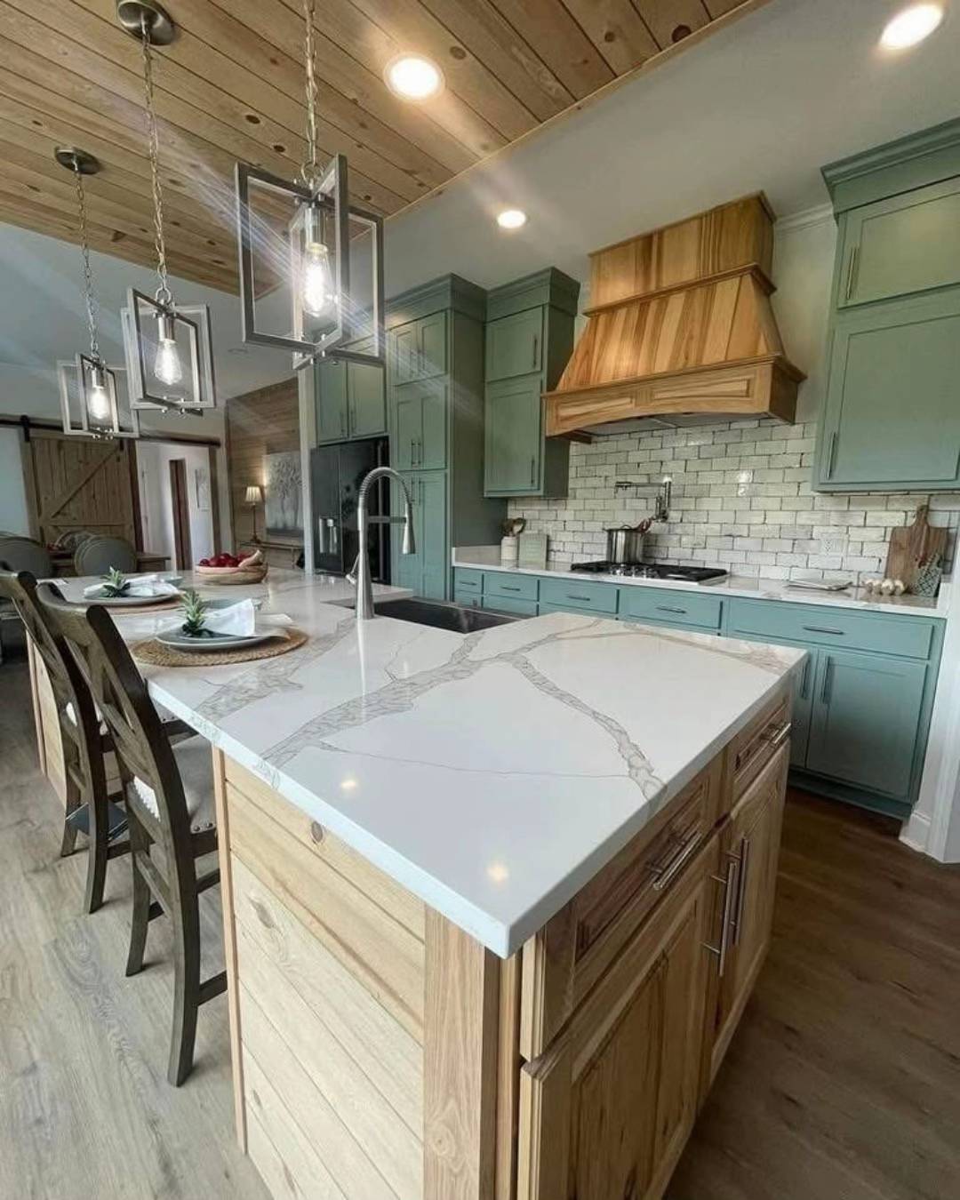 Modern kitchen with light wood floor and ceiling, green cabinets, white marble countertops, and pendant lights. Cozy and inviting atmosphere.